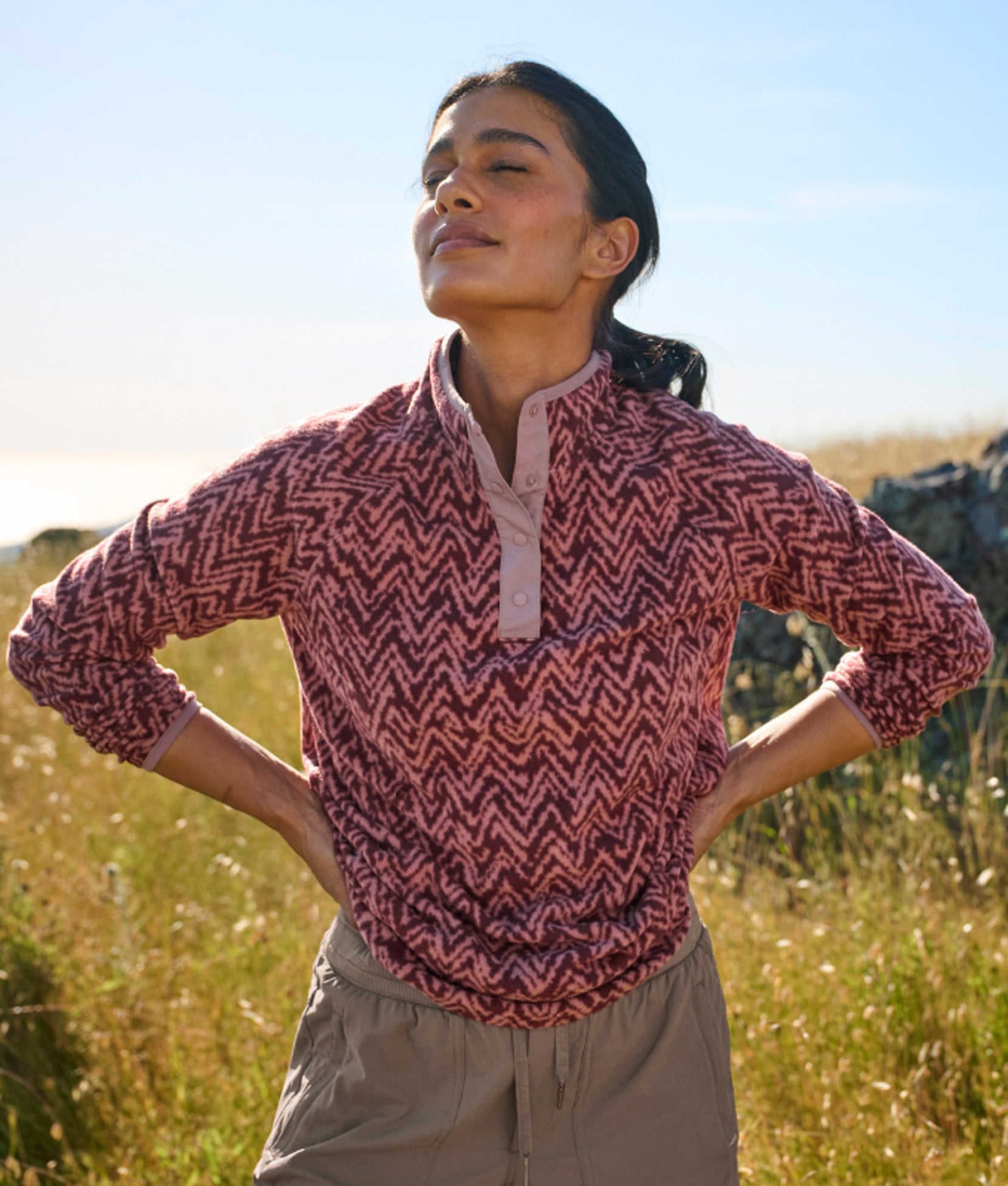 A woman in a field, outdoors wearing a patterned quarter-zip fleece pullover.