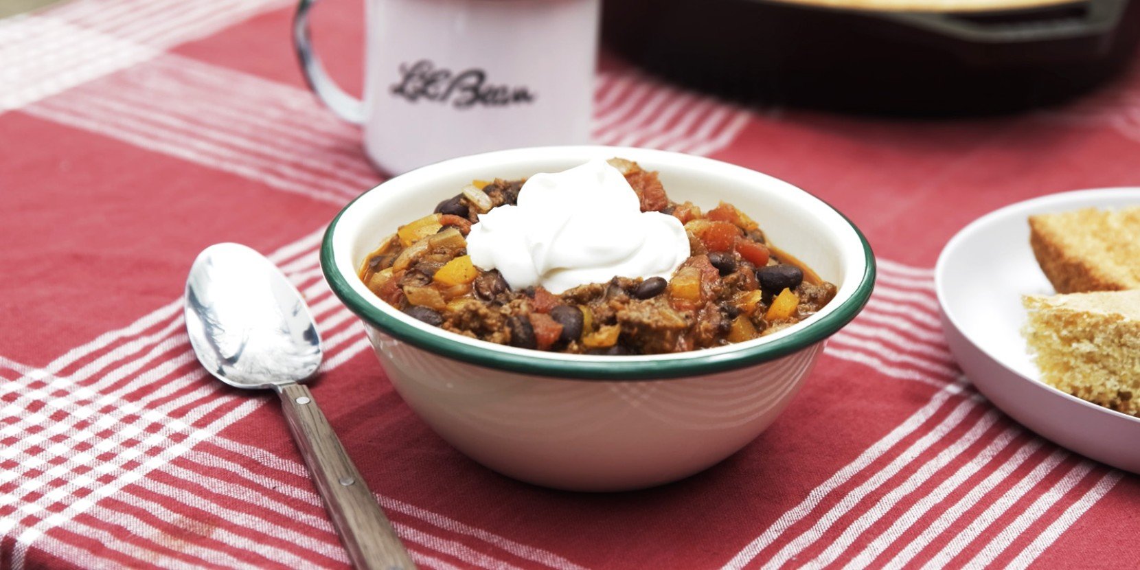 A bowl of chili with a dollop of sour cream on a red and white checkered tablecloth.
