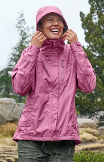 Person wearing a pink rain jacket with the hood up, standing outdoors in light rain.