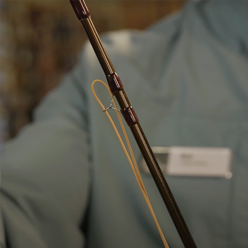 Close-up of a person holding a fishing rod with a yellow line looped through the guides.