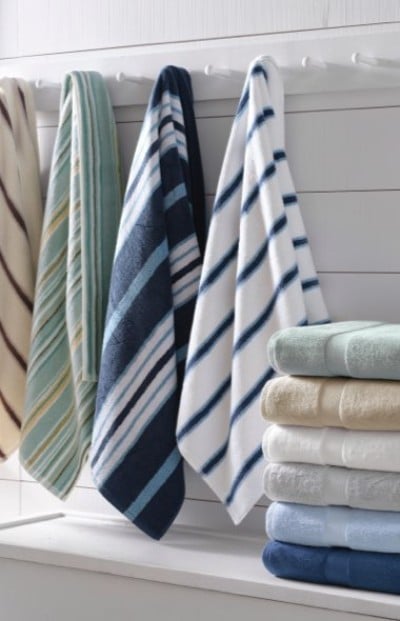 Stack of colorful folded towels on a white table; four striped towels hang on the left against a white wooden wall.