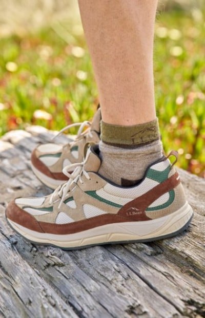 Sneaker with brown and green accents worn on a weathered wooden surface.