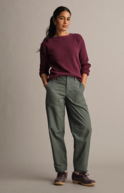 Person wearing a burgundy sweater and green pants standing in a studio setting.