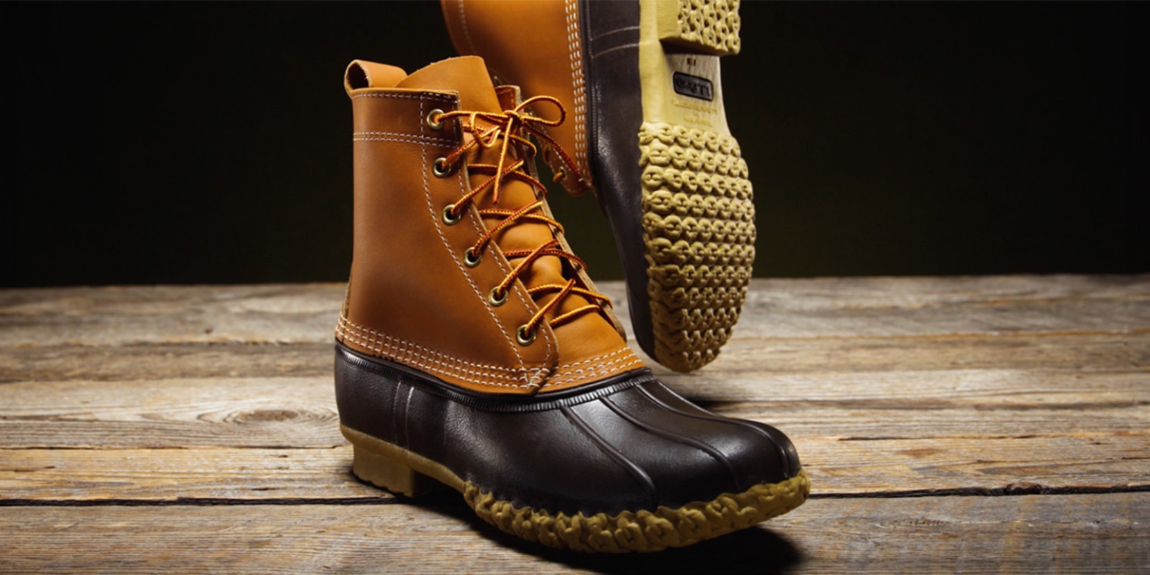 A pair of L L Bean boots with yellow laces, displayed on a wooden surface.