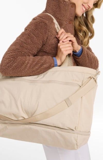 Beige weekender bag carried over the shoulder by someone wearing a textured brown fleece jacket.