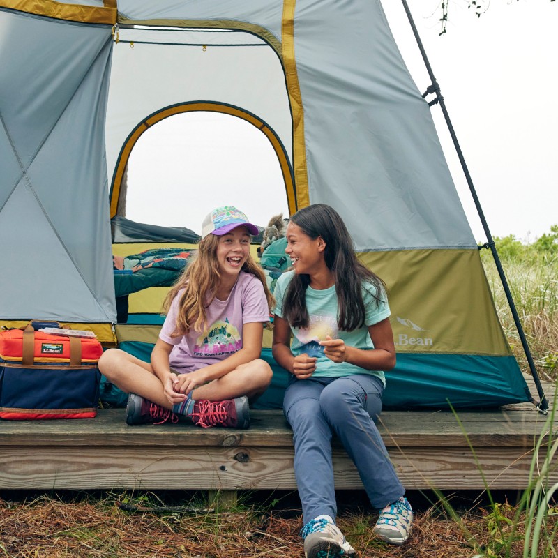 Two smiling young girls sitting by a tent.