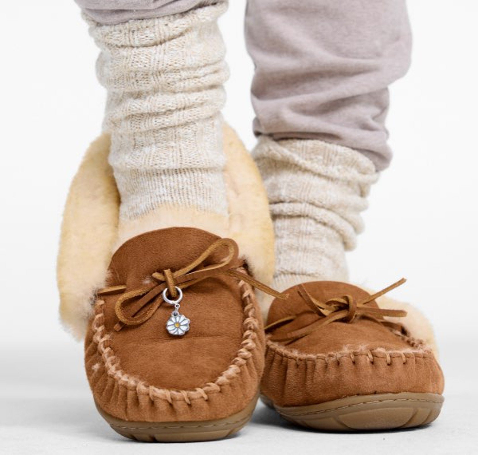 Person wearing brown shearling-lined moccasin slippers with socks on their feet. 