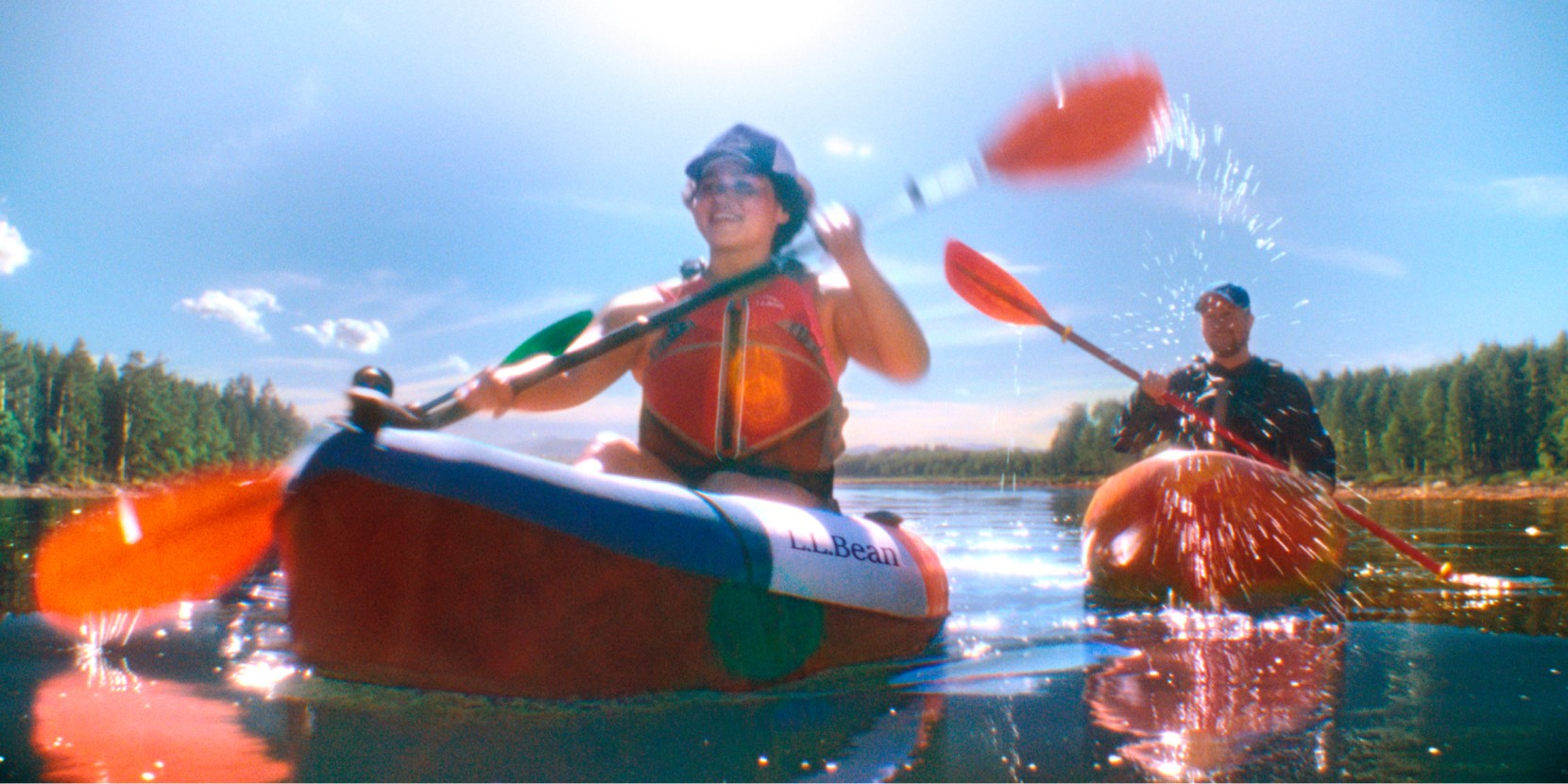 A woman and a man paddling in kayaks on a bright, sunny day.