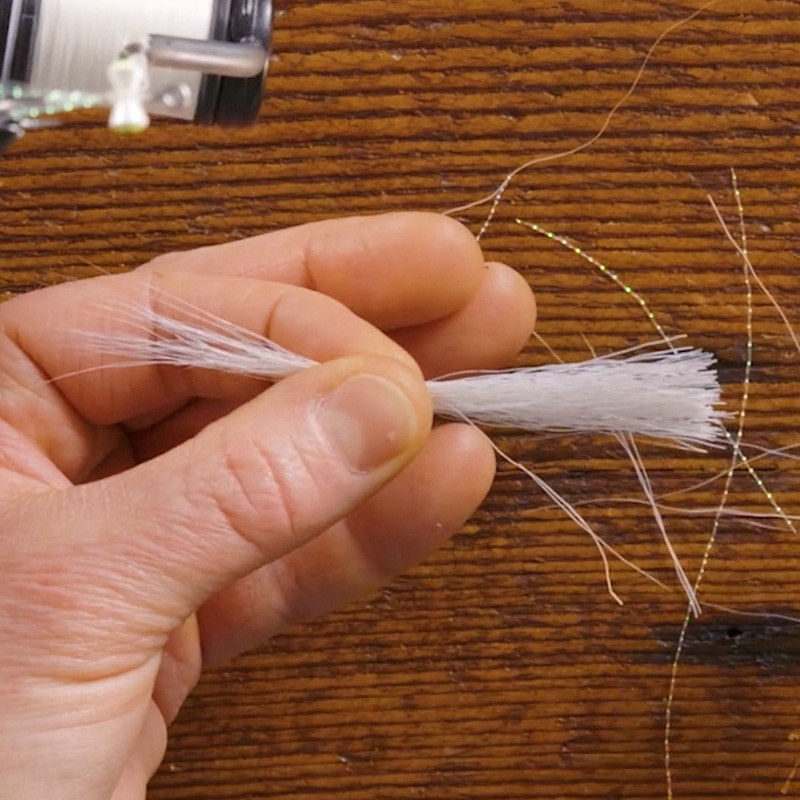 Hand holding white synthetic fibers called bucktail for fly tying.