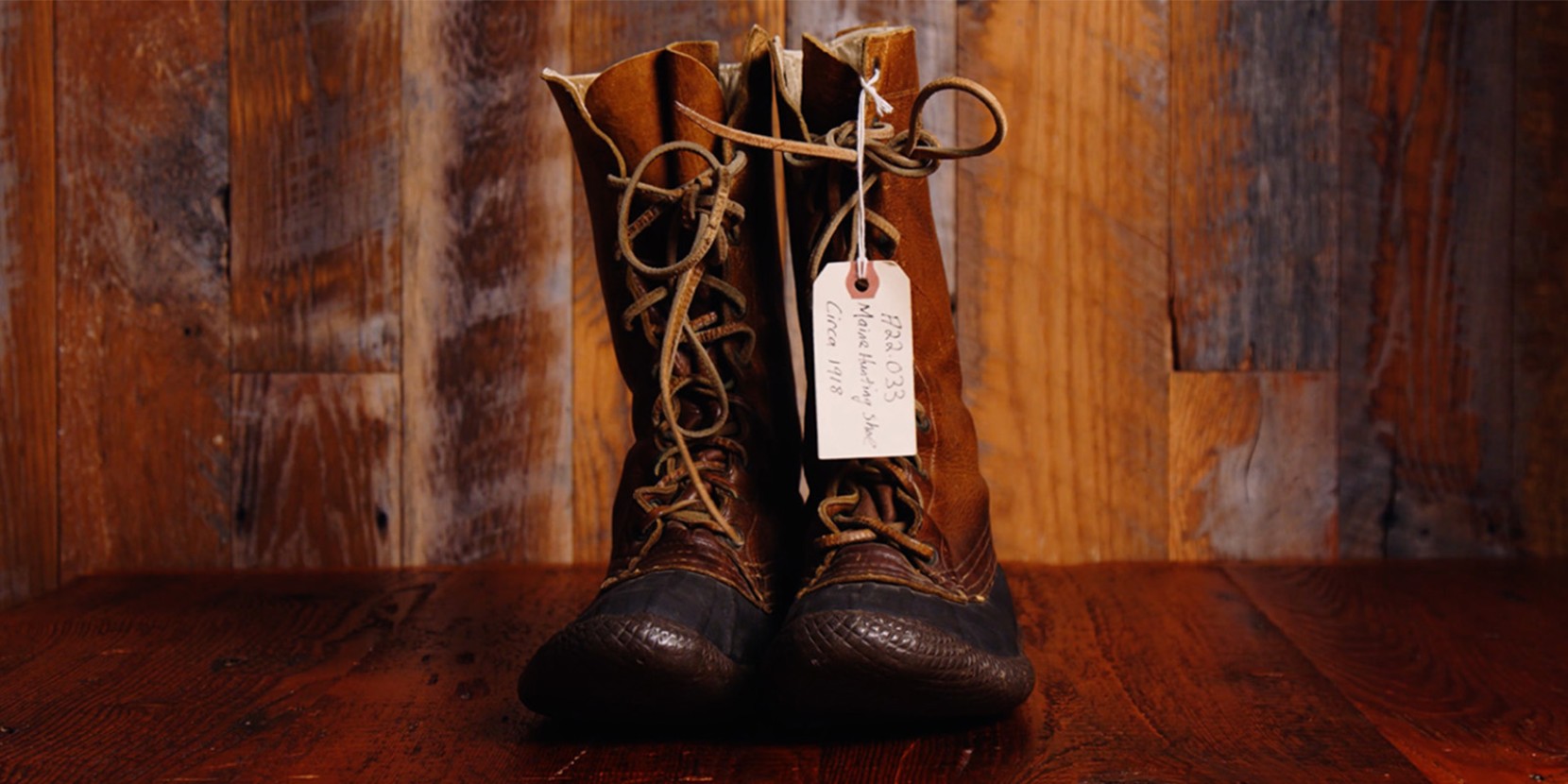 Vintage L L Bean boots labeled F22.033 Maine Hunting Shoe Circa 1918 displayed on wood with a rustic background.