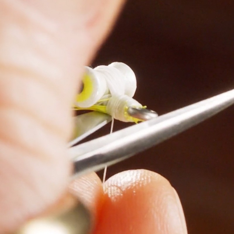 Close-up of a person using scissors to cut a thin white thread near a fishing fly.