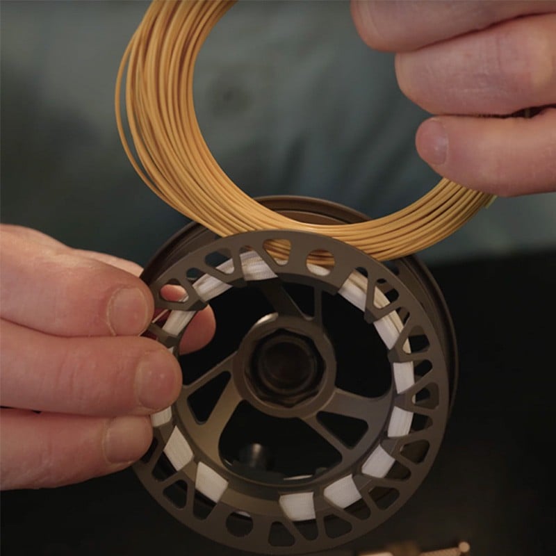 Person holding a spool of yellow filament and a reel, preparing to load the filament onto the reel.