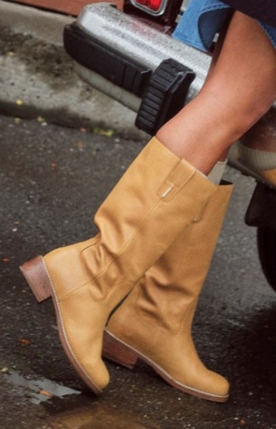 Close up of tan heeled mid-calf boots stepping out of a vehicle onto pavement.