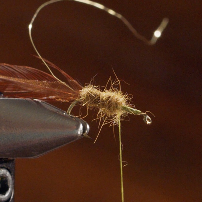A fly fishing lure in a vise, with feathers and thread being tied.