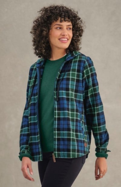 Woman in blue and green plaid jacket over green sweater stands against a plain background. 