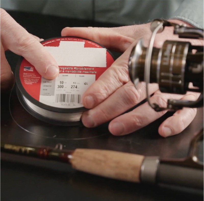 A person holds a spool of fishing line labeled 