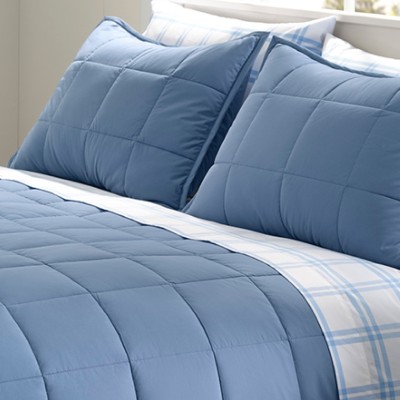 A neatly folded bed with a plush, blue comforter and matching pillows.