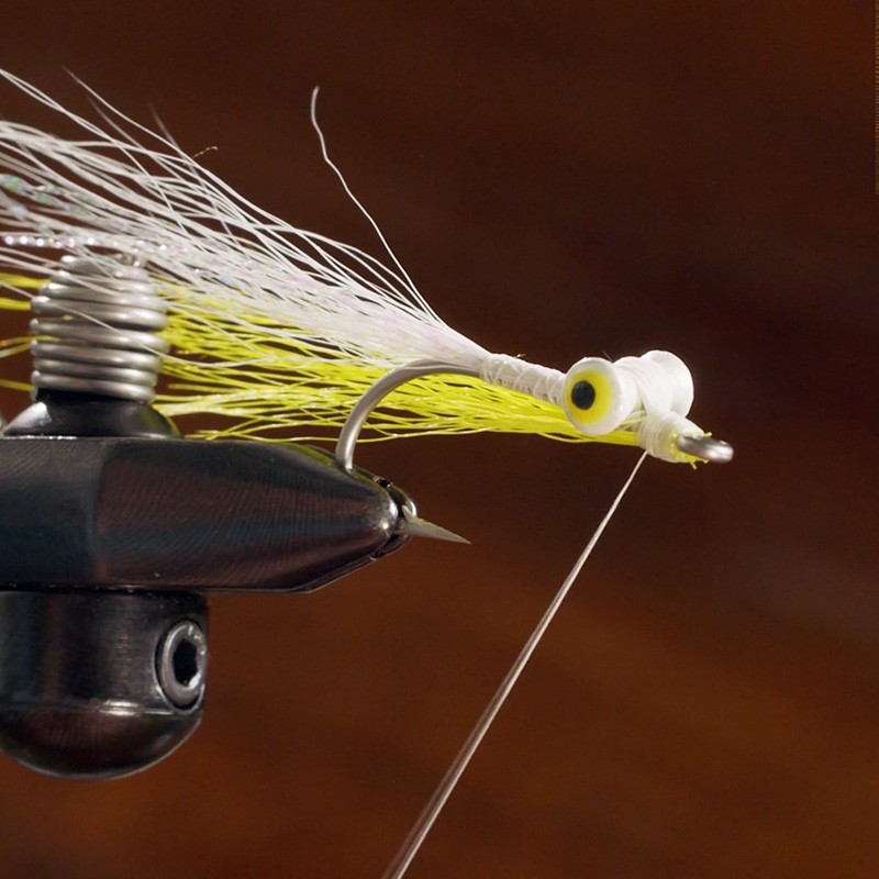 Close-up of a fishing fly being tied, featuring a hook, synthetic fibers, and a vise holding the hook in place.