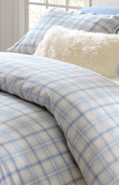 Light blue plaid comforter with a soft white accent pillow on a neatly styled bed.