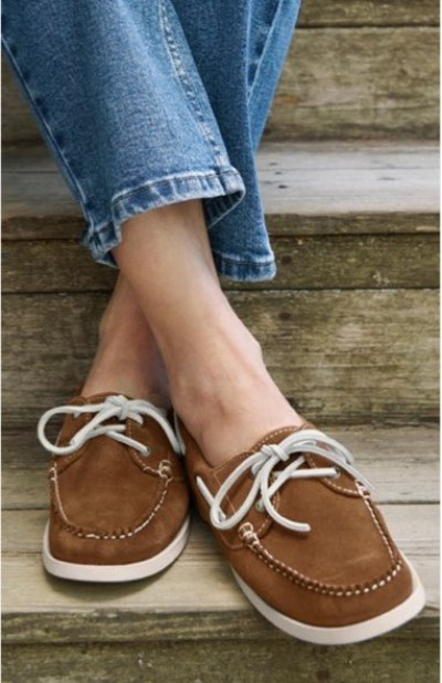 Close up of a person wearing brown boat shoes with white laces on wooden steps.