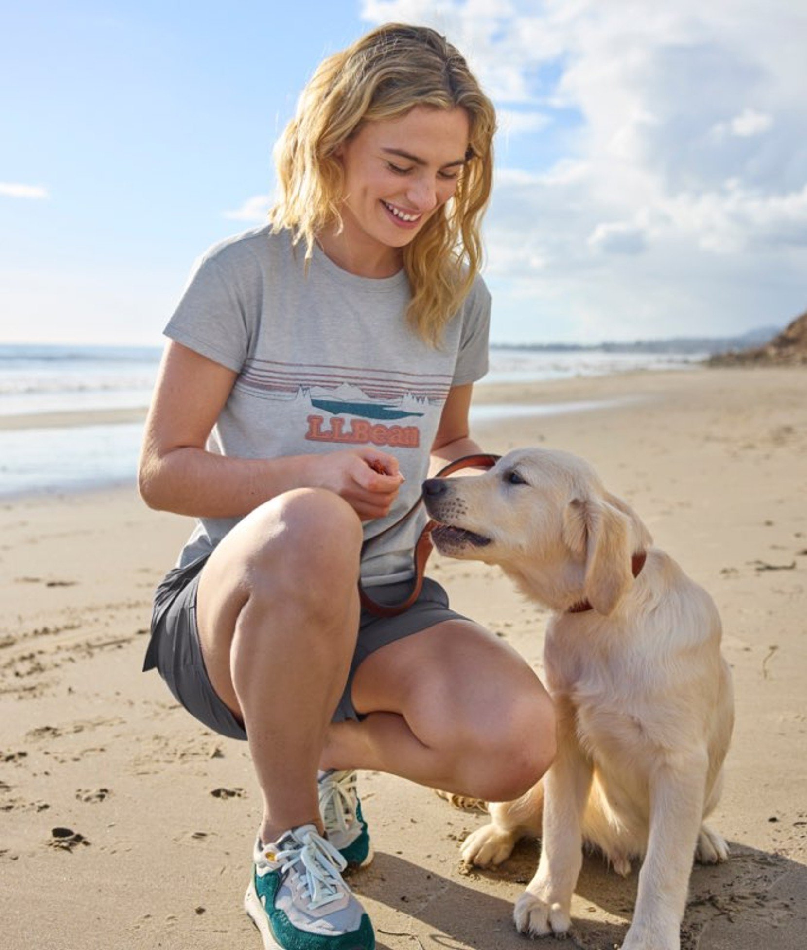 Person sitting outdoors wearing casual clothing, interacting with a small dog in a natural setting. 
