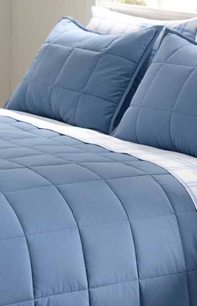 A neatly folded bed with a plush solid blue comforter and pillows.
