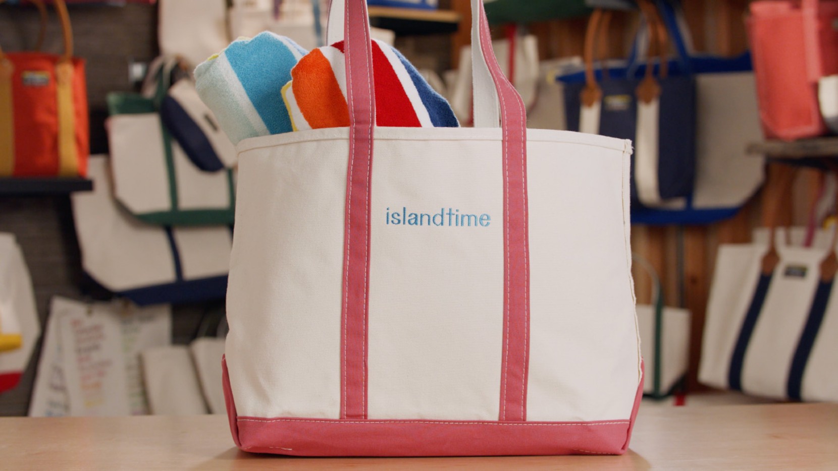 A large Boat & Tote with red handles and light blue monogram - islandtime, filled with towels and beach toys.