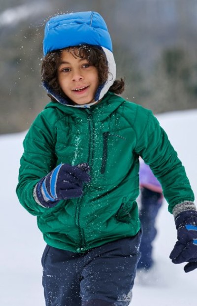 Child running through snow wearing a green jacket, blue hat, and gloves.