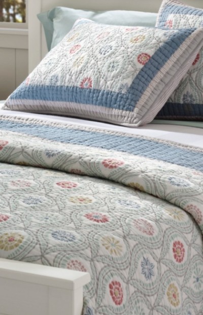 A neatly folded bed with matching bed spread, quilt and pillow.