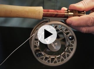 Close-up of a person holding a fishing rod with a reel labeled APEX 2 and an overlaying play video icon.