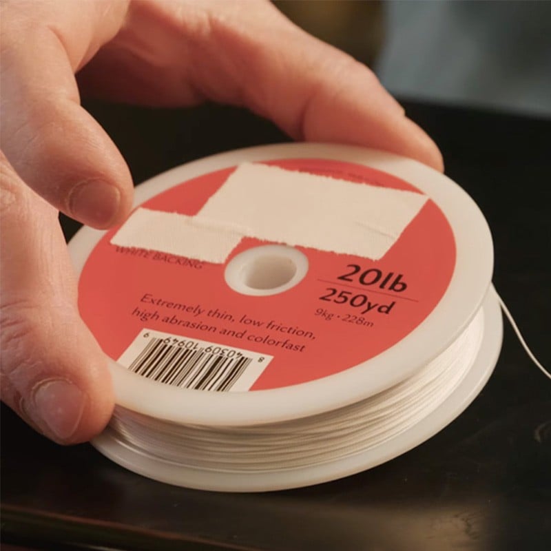 A hand holding a spool of fishing line labeled 20 pounds and 250 yards.