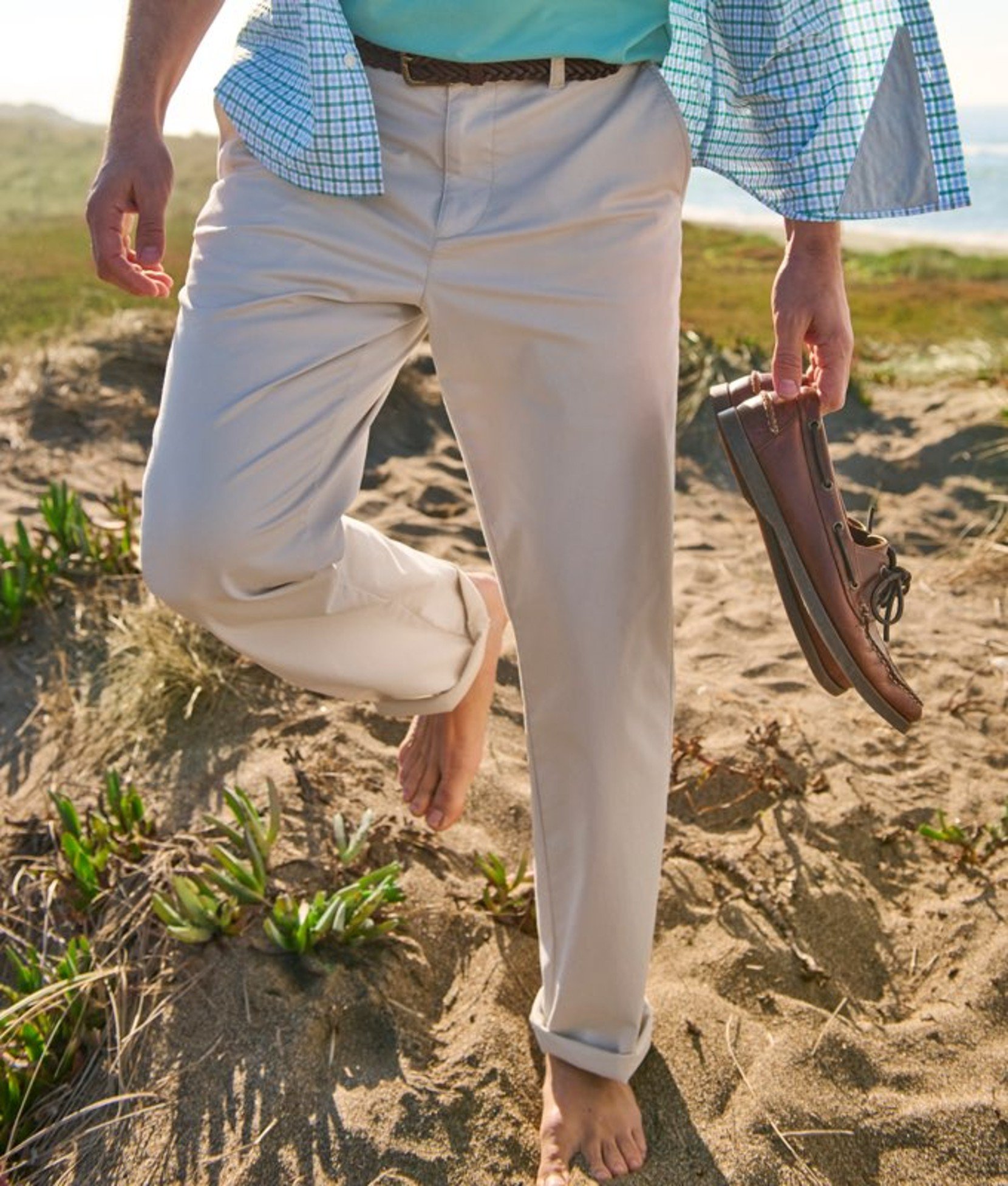 Person wearing rolled-up pants outdoors near greenery and sand, suggesting a coastal setting.