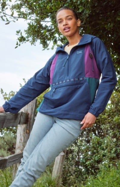 Person standing outdoors in a blue and purple pullover jacket with trees in the background.