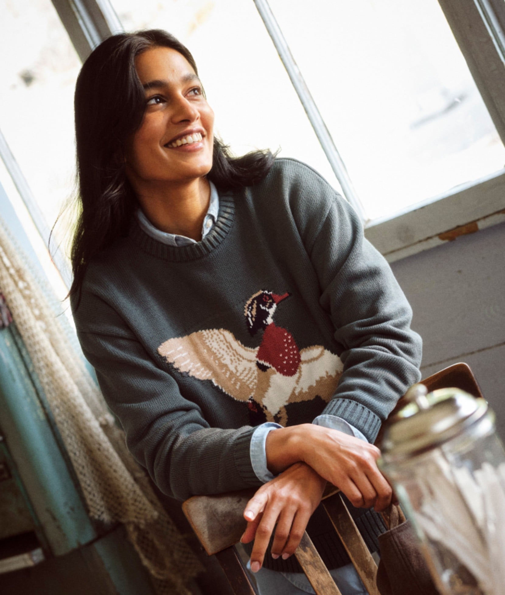 Woman seated aboard a boat wearing a sweater with a bird motif.