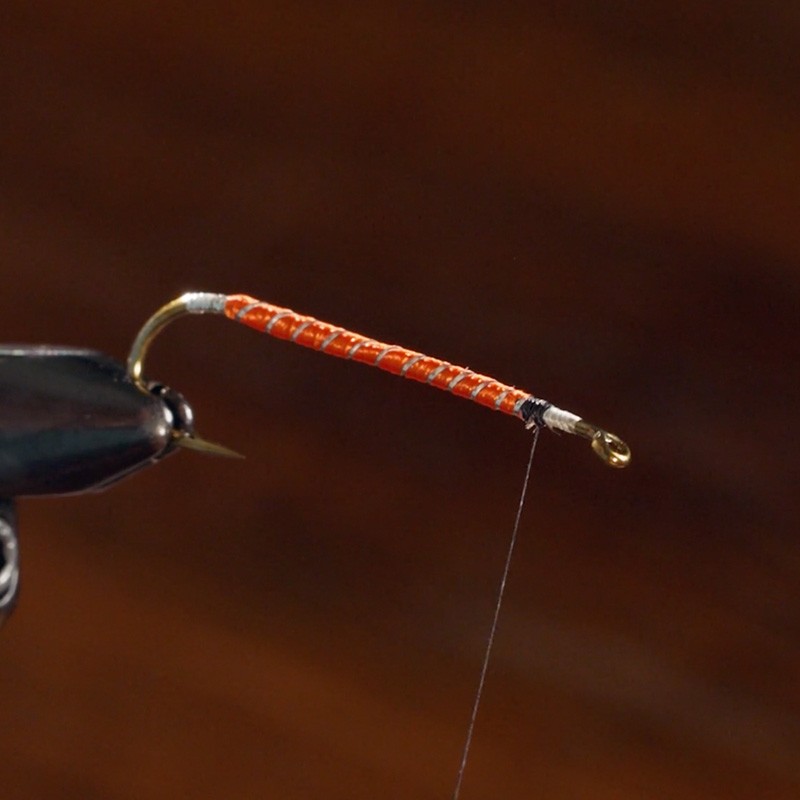 Copilot Close-up of a fishing fly hook with an orange and white wrapped body, black thread, and a gold eyelet.
