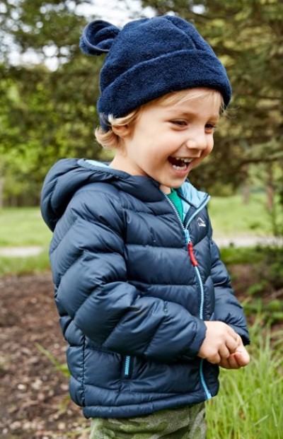 Young child in a navy puffer jacket and knit hat standing outdoors.