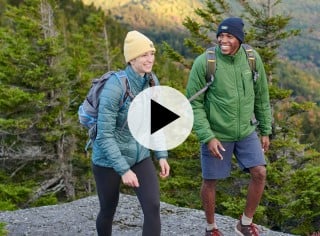 2 people hiking, a play video icon in the center.