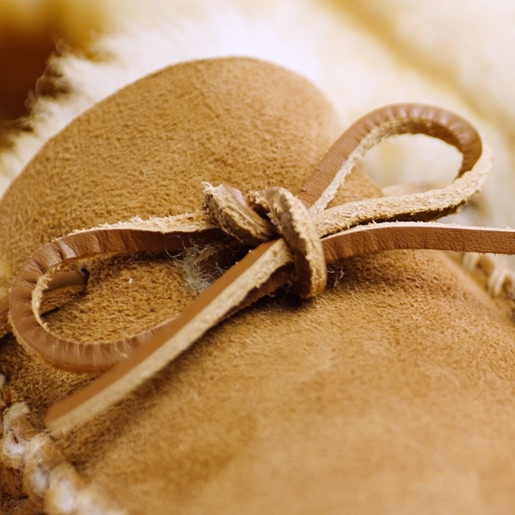 Close-up of a tan suede moccasin slipper with a tied leather lace and soft fleece lining visible in the background.