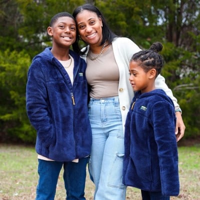 A woman outside with her arms around two kids.