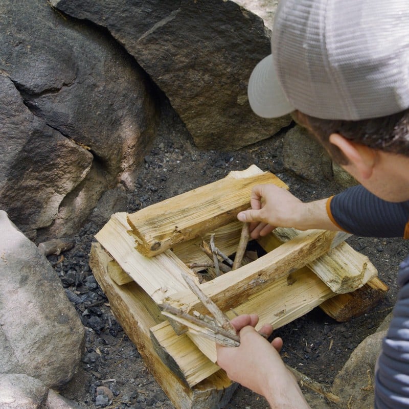 Nate placing small kindling in the center of several layers of log-cabin style stacked fuel logs.