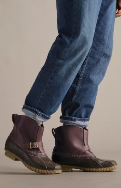 Cropped image of legs wearing brown leather Chelsea boots with rolled jeans standing on a neutral studio floor.