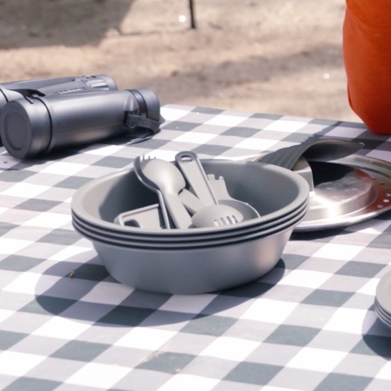 Outdoor picnic setting with utensils and bowls on a checkered tablecloth, ready for a meal.