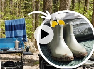 A camping scene with a blue-striped towel, cooking gear on a table, and muddy boots, with a play video icon.