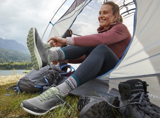 Woman putting on her hiking shoes while sitting in a tent.