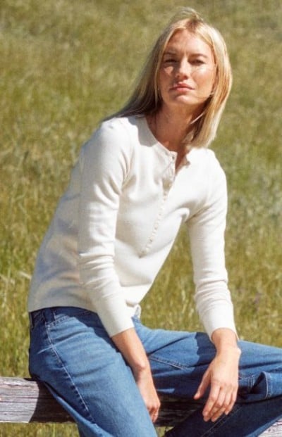 Person seated in a grassy field wearing a white long-sleeve henley shirt.