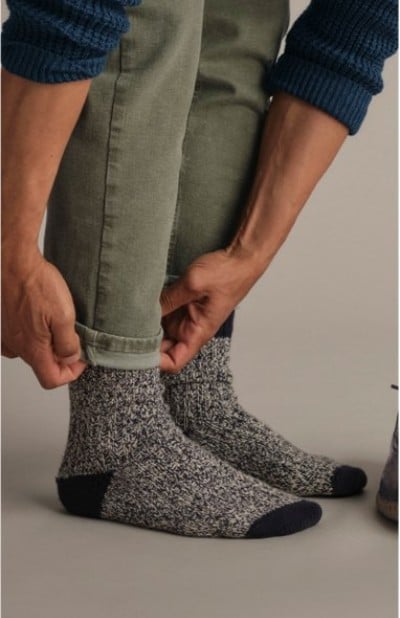 Person rolling up pant cuffs while wearing thick gray and black knit socks.