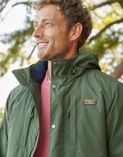 Person outdoors wearing a green hooded jacket over a orange sweater.