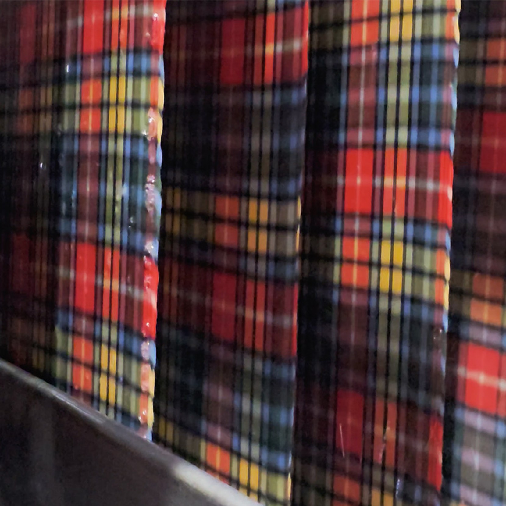 Plaid fabric with red, yellow, blue, and black stripes, shown with vertical folds.