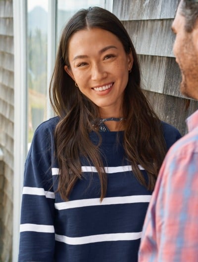 Woman in a striped navy pullover stands outside near a shingled wall. 