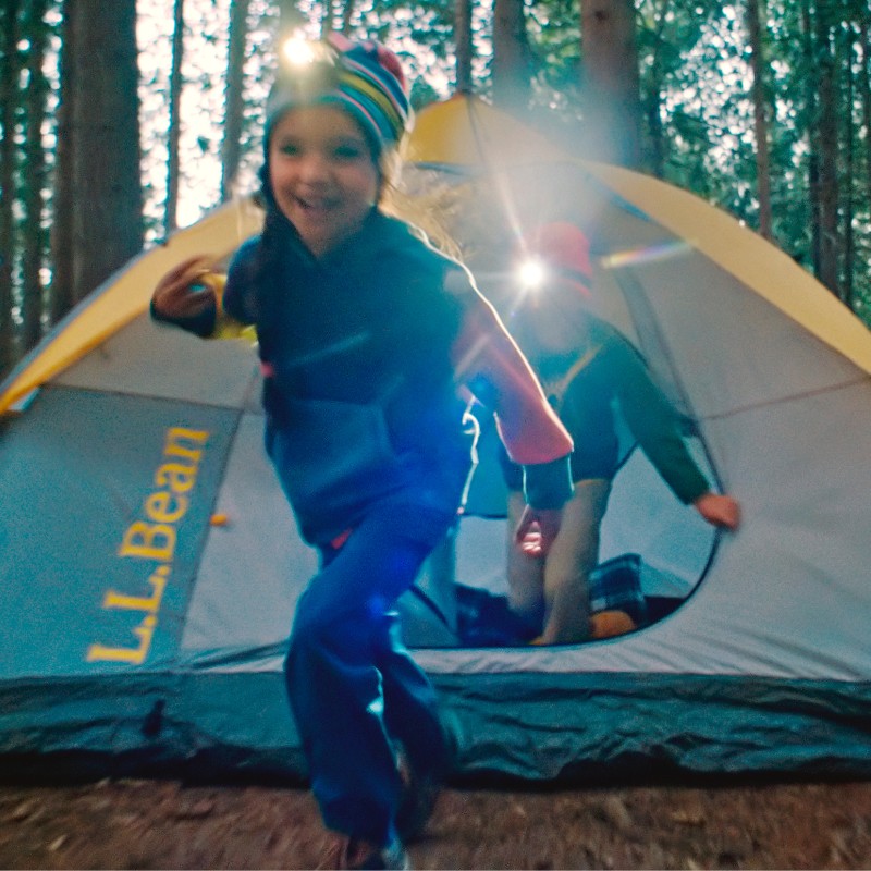 Two happy kids coming out of tent with headlamps on.